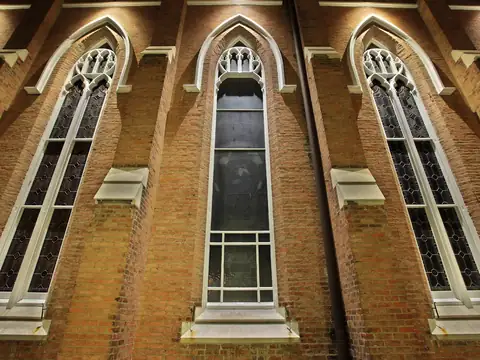 Brick church elevation with arched windows grazed by warm light
