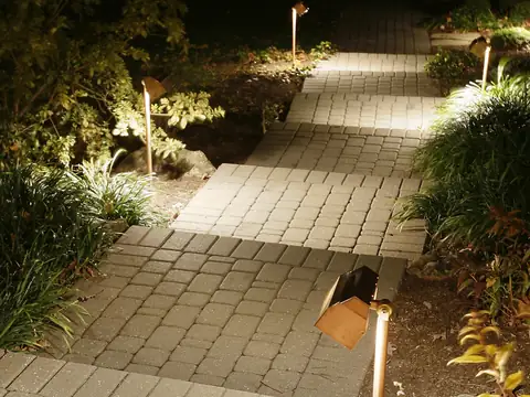 Paver walkway lit by low path fixtures through planted beds